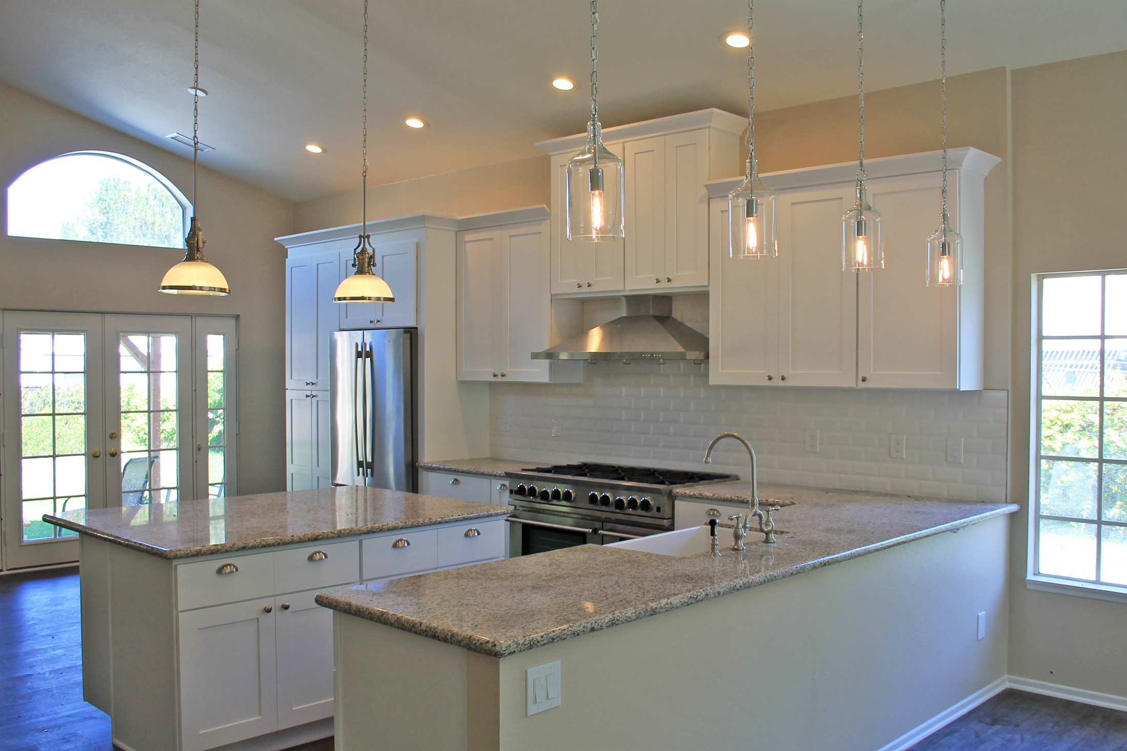 High-ceiling open-concept kitchen with white cabinetry, pendant lights, and professional range