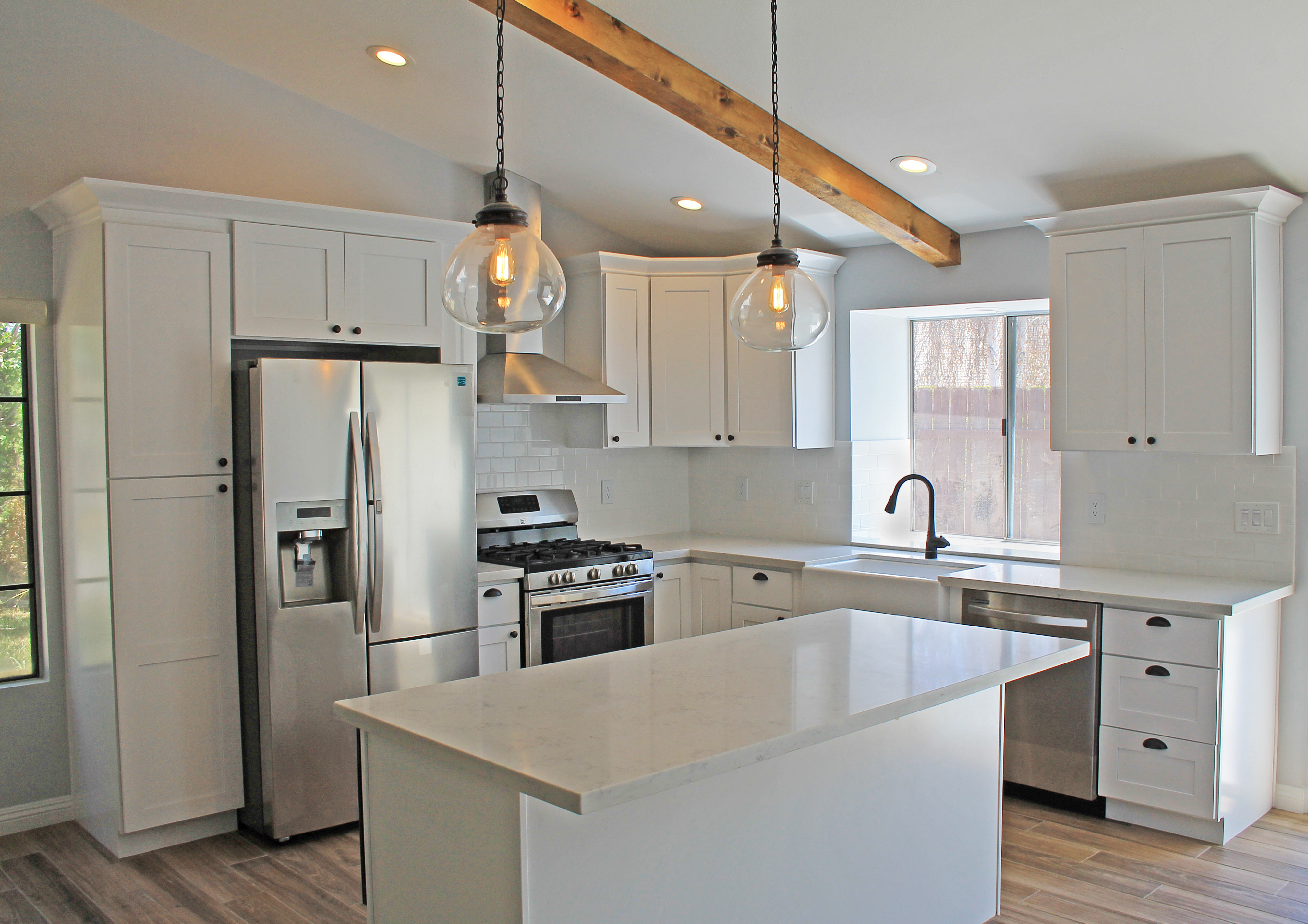 Modern farmhouse kitchen with white shaker cabinets, quartz counters, exposed wood beam, and subway tile