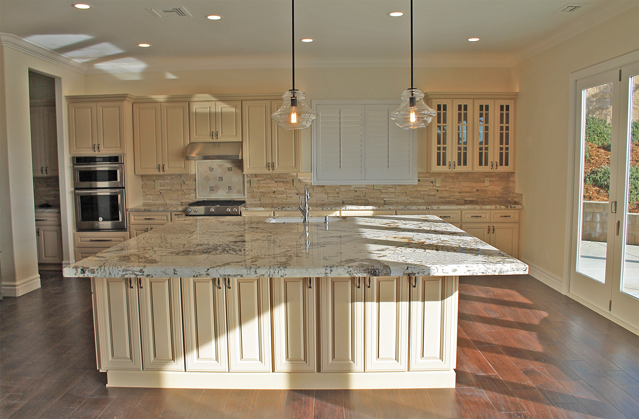 Kitchen with massive granite island, cream cabinetry, stone backsplash, pendant lights, and hardwood floors